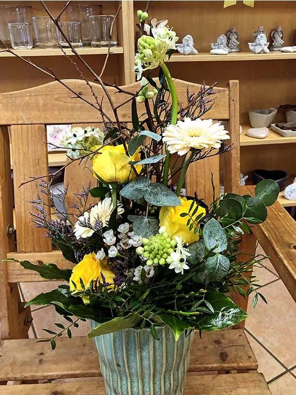 Auf einem Holzstuhl steht eine Vase mit gelben und weißen Blumen.