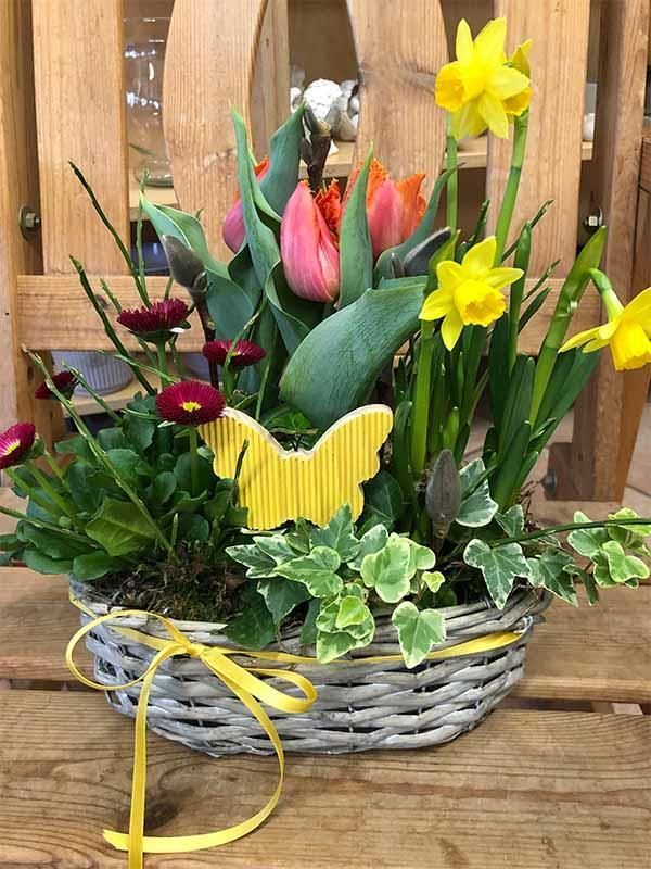 Ein Korb voller Blumen und ein gelber Schmetterling auf einem Holztisch.