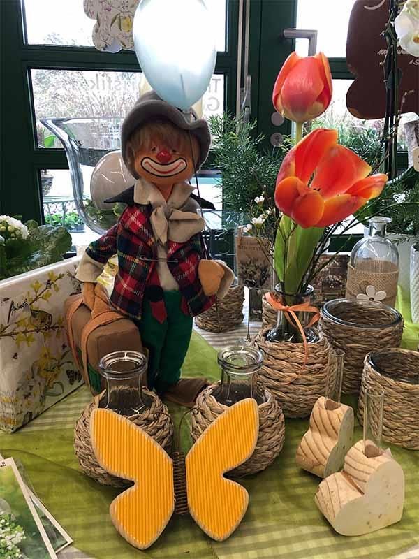 Ein Clown sitzt auf einem Tisch mit Blumen und einem Schmetterling.