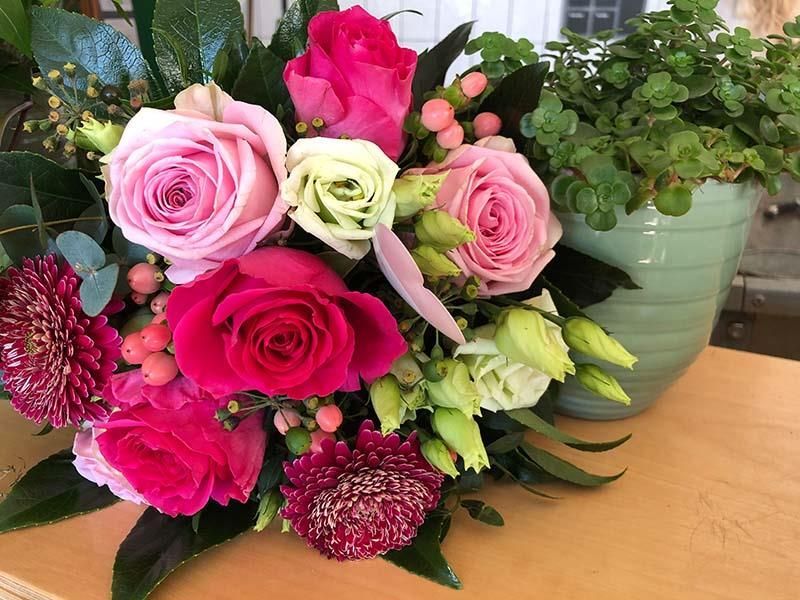 Ein Strauß rosa Rosen steht auf einem Tisch neben einer grünen Topfpflanze.