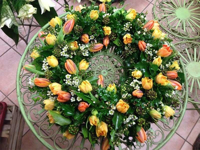 Ein Kranz aus gelben und orangen Blumen auf einem grünen Tisch