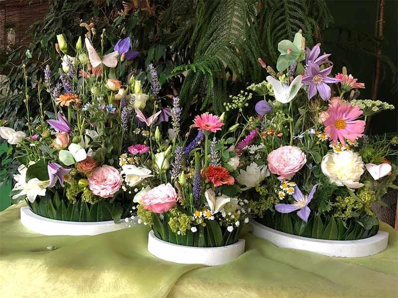 Auf einem Tisch stehen drei mit Blumen gefüllte Vasen.