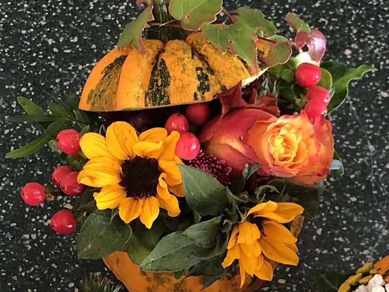 Ein Kürbis gefüllt mit Sonnenblumen und Beeren auf einem Tisch