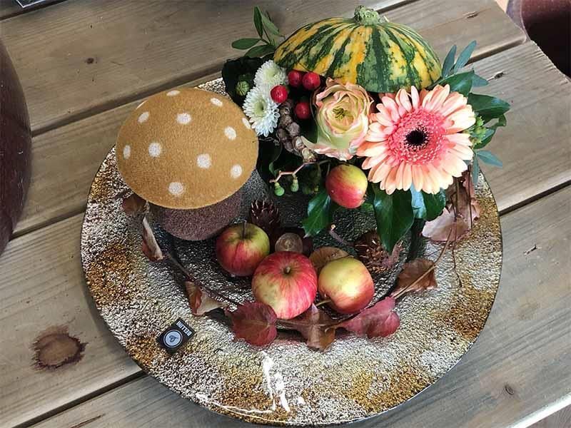 Ein Teller mit Blumen und Äpfeln auf einem Holztisch.