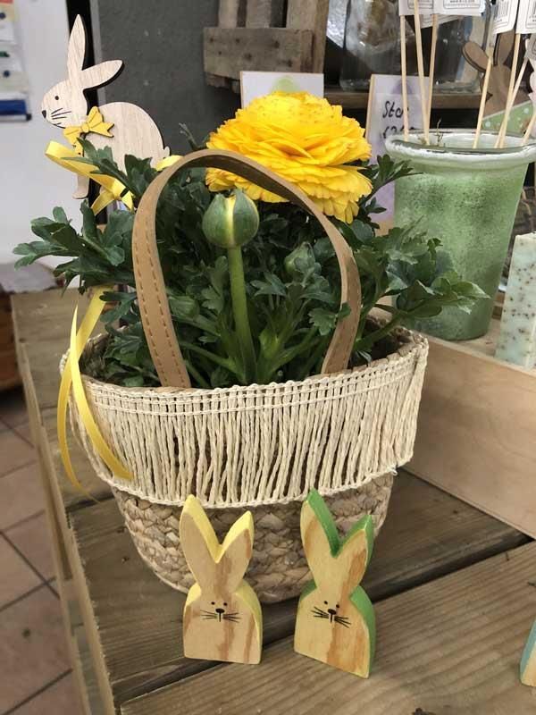 Ein Korb voller gelber Blumen und Holzhasen auf einem Tisch.