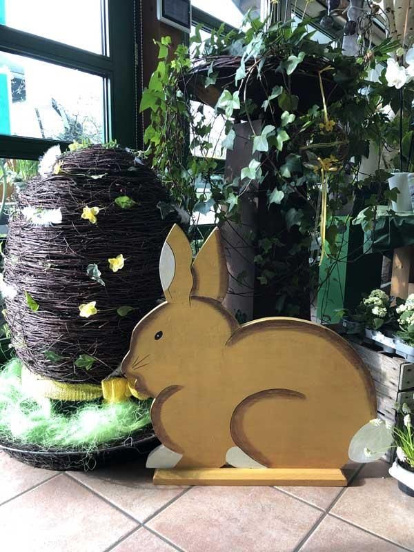 Ein Holzhase sitzt neben einem großen Weidenei.