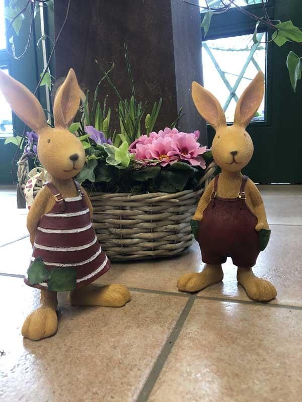 Ein paar Hasenfiguren stehen neben einem Blumenkorb
