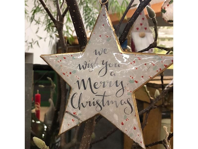 An einem Ast hängt ein Stern mit der Aufschrift „Wir wünschen Ihnen frohe Weihnachten“.