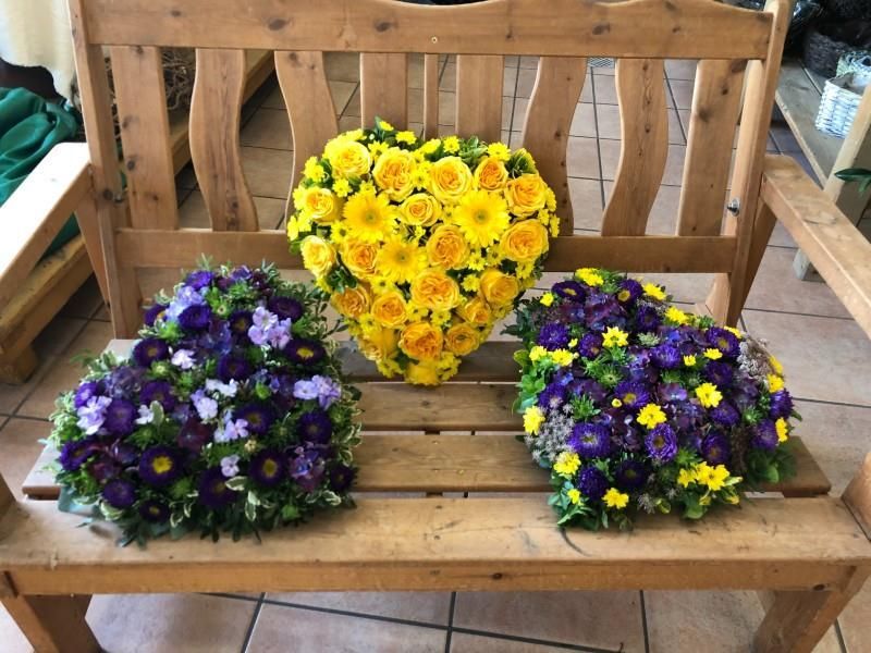 Drei herzförmige Blumen sitzen auf einer Holzbank