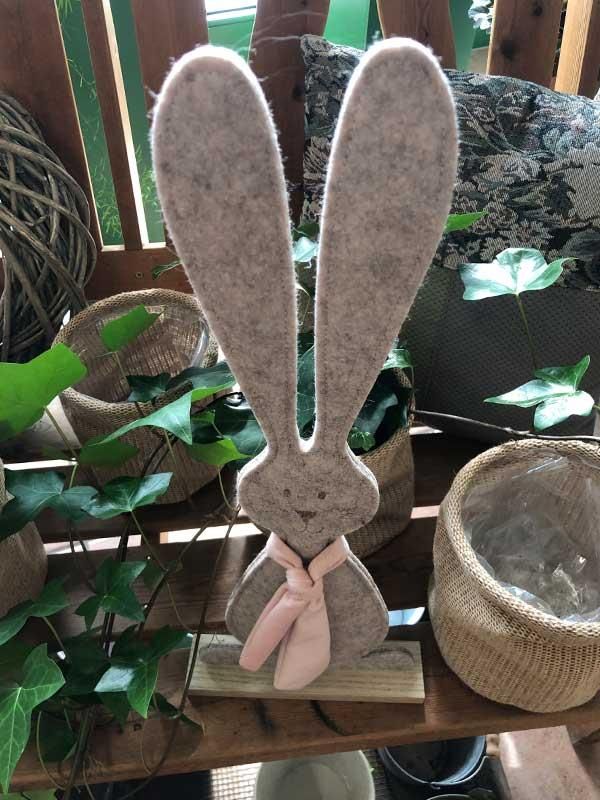 Ein Hase mit einer rosa Schleife sitzt auf einem Holzregal.