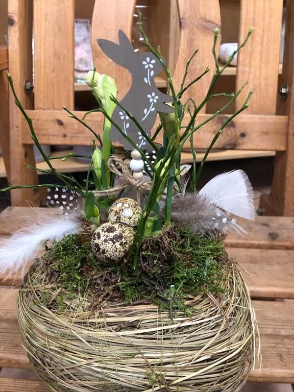 Auf einem Holztisch steht ein Korb voller Blumen und Federn.
