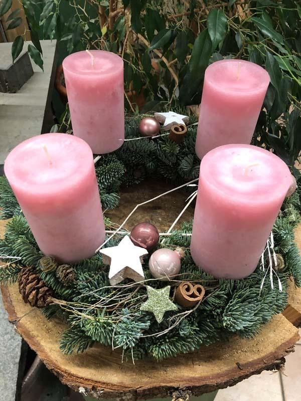 Ein Weihnachtskranz mit rosa Kerzen und Tannenzapfen auf einem Holztisch.
