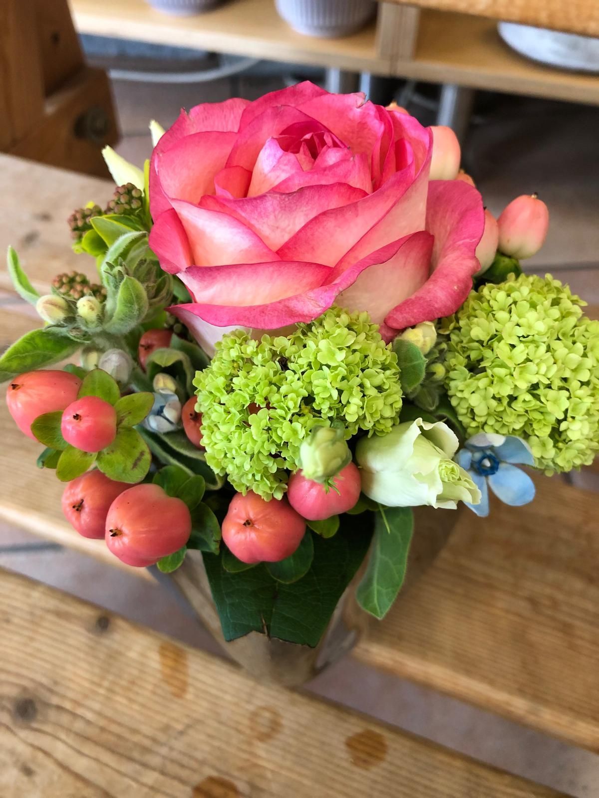 Eine große rosa Rose in einem Gesteck mit Zieräpfeln und Hortensie