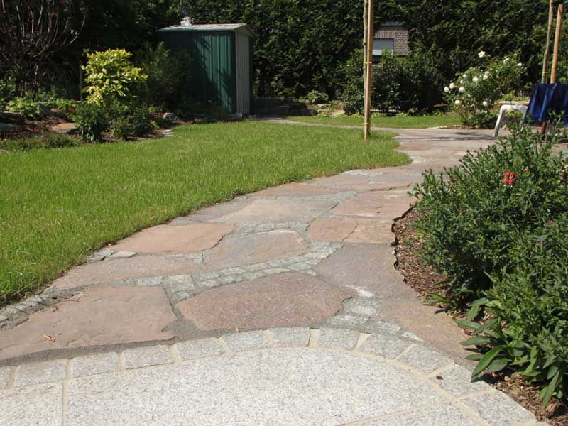 Ein Steinweg in einem Garten mit einem grünen Schuppen im Hintergrund