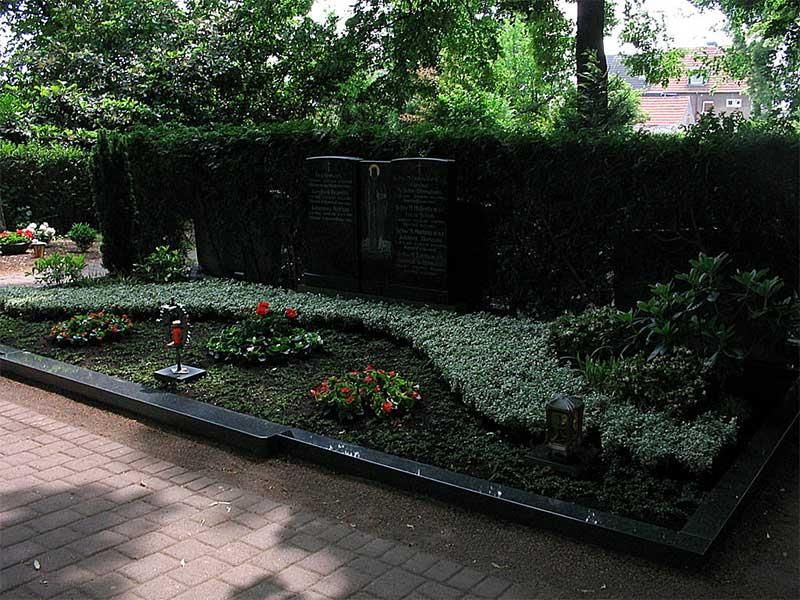 Ein Grab auf einem Friedhof mit Blumen und einer Hecke