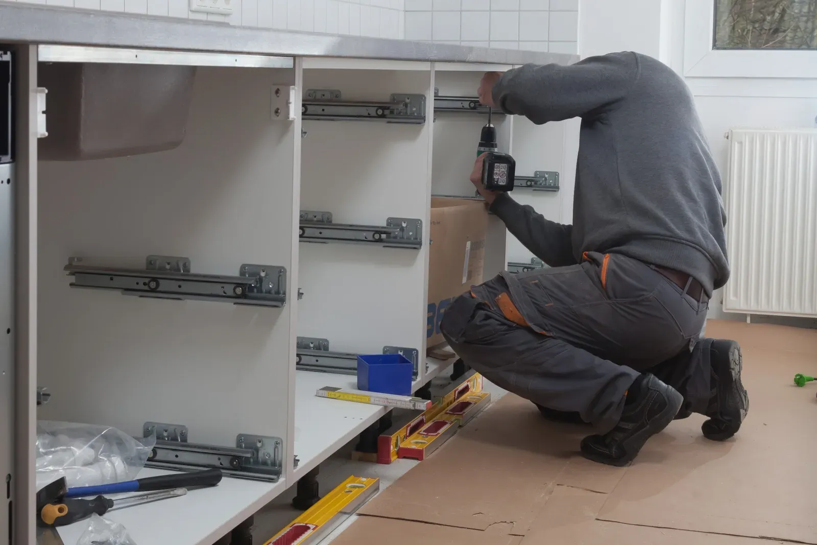 Ein Mann bearbeitet mit einer Bohrmaschine einen Küchenschrank.