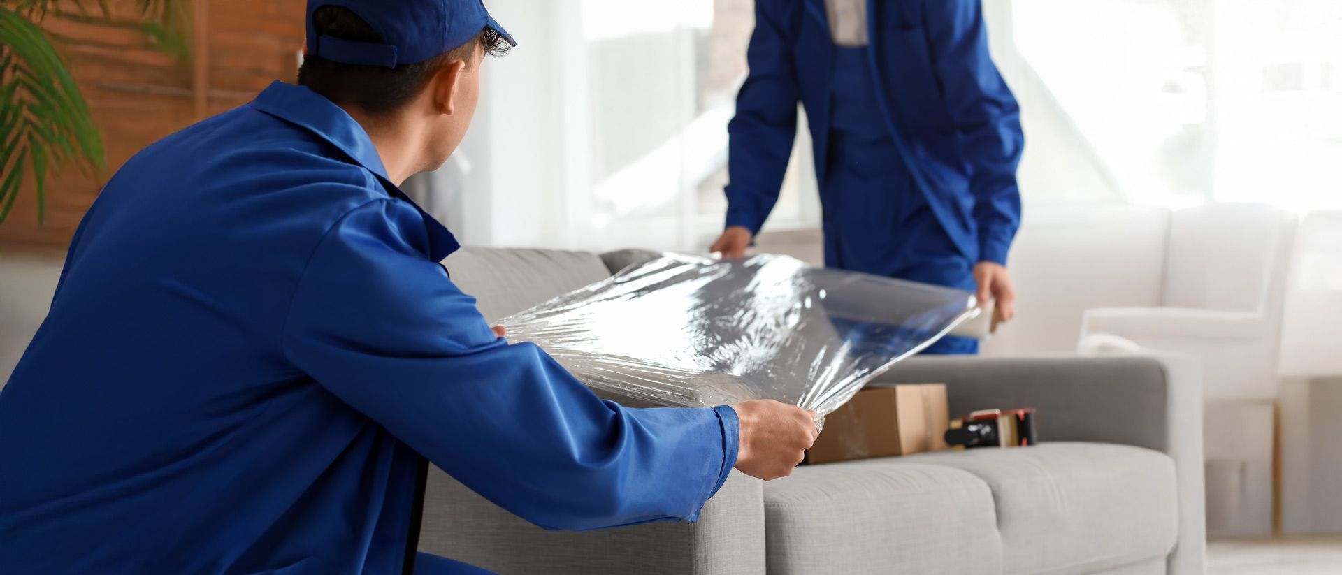 Zwei Möbelpacker verpacken ein Sofa in Plastikfolie.