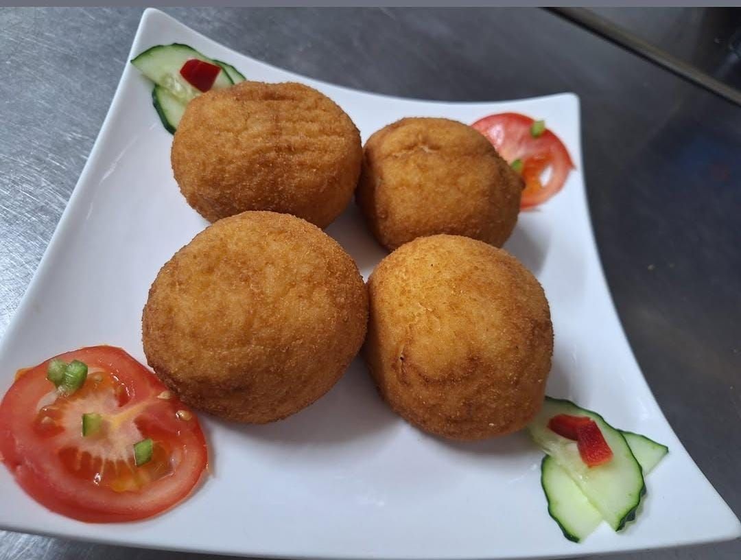 Cuatro bolas fritas en un plato blanco con tomates y pepinos.