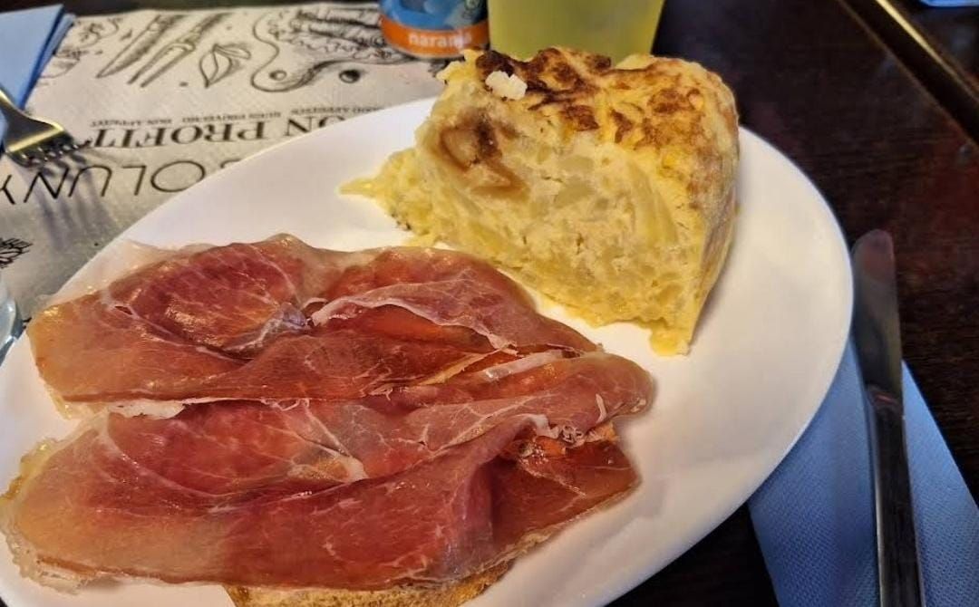 Un plato blanco cubierto con carne y pan sobre una mesa.