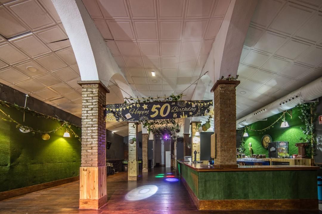 Salón de fiestas decorado para celebrar 50 cumpleaños con bar, paredes verdes y luces de colores.