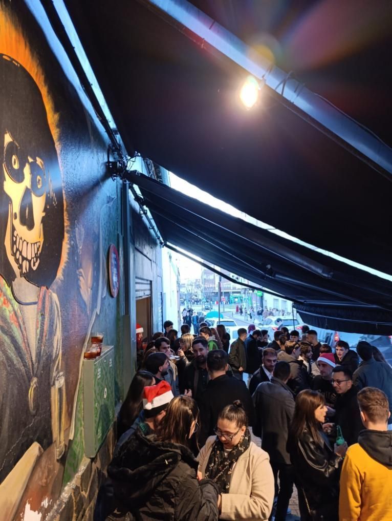 Una multitud de personas bajo un toldo, cerca de un mural de una figura con cara de calavera.