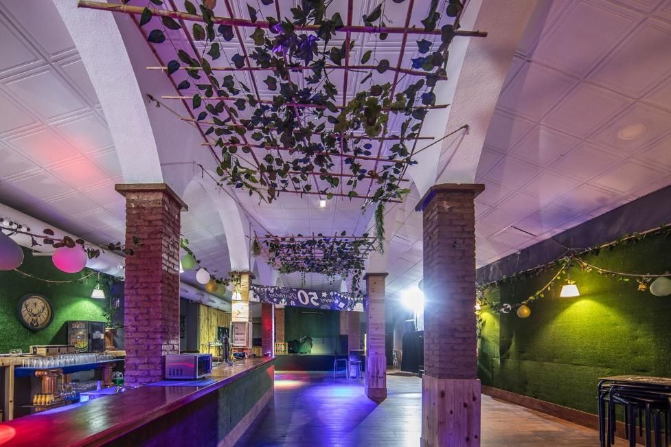 Interior de un espacio para eventos decorado con bar y vegetación artificial.