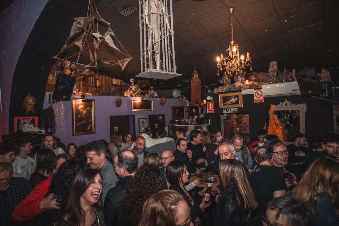 Un bar abarrotado y con poca luz. La gente se mezcla, ríe y charla bajo una decoración gótica y una lámpara de araña.