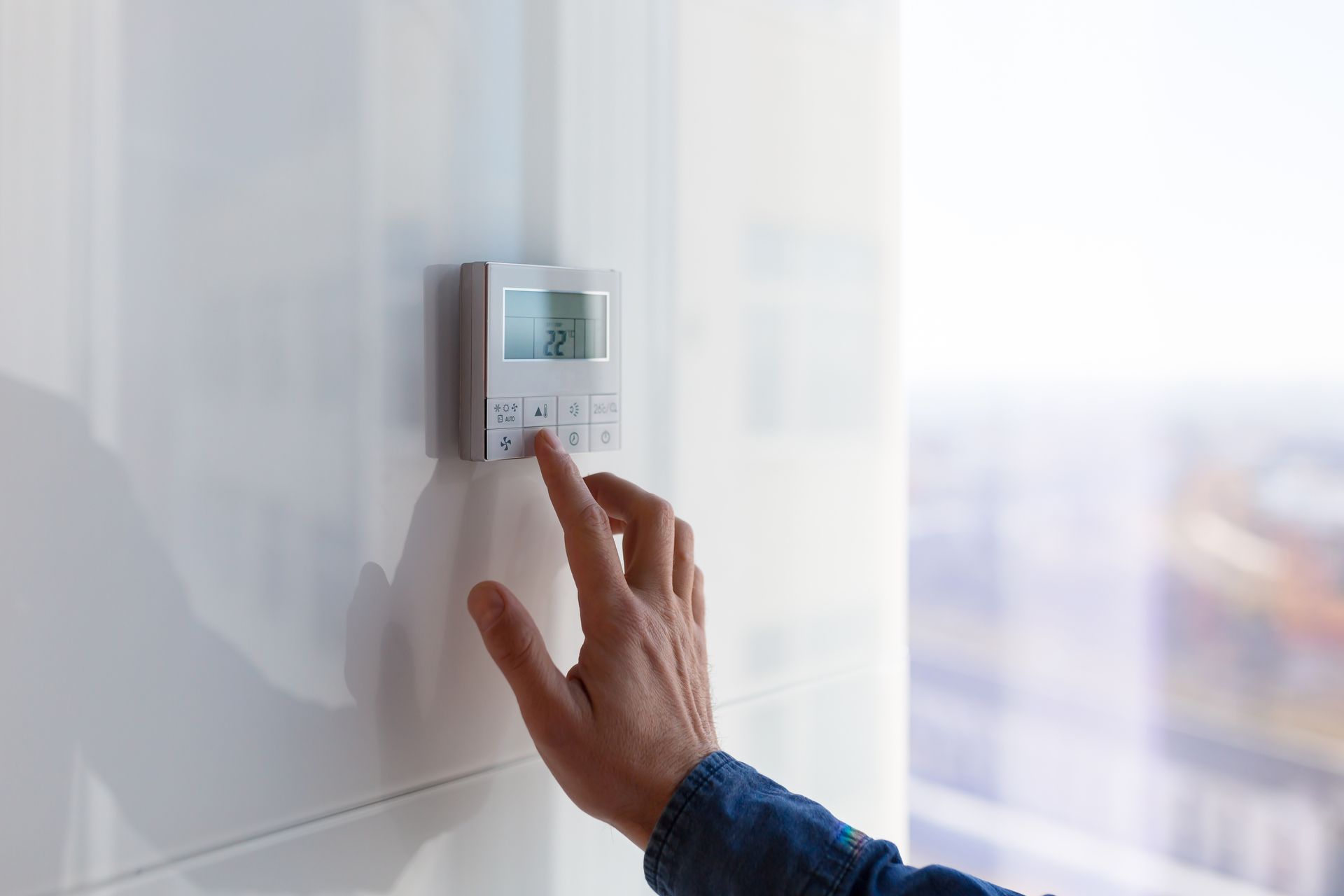 Une main tapant sur le clavier d'un thermostat de maison.