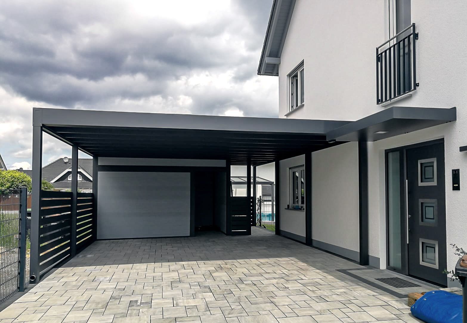 Modernes Carport am Haus mit schwarzem Vordach, Garagentor, gepflasterter Einfahrt und Eingangstür