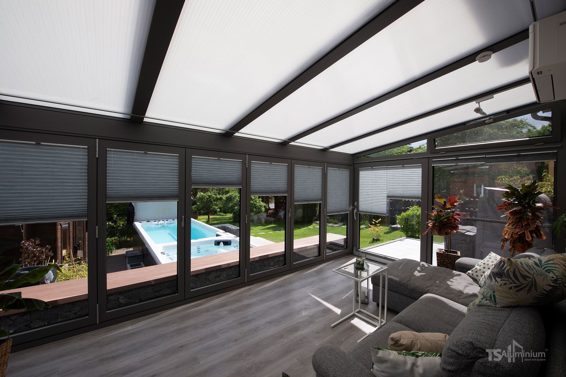 Moderner Wintergarten mit Glaswänden, Lounge-Sitzgelegenheiten und Blick auf einen Pool und Garten im Hinterhof