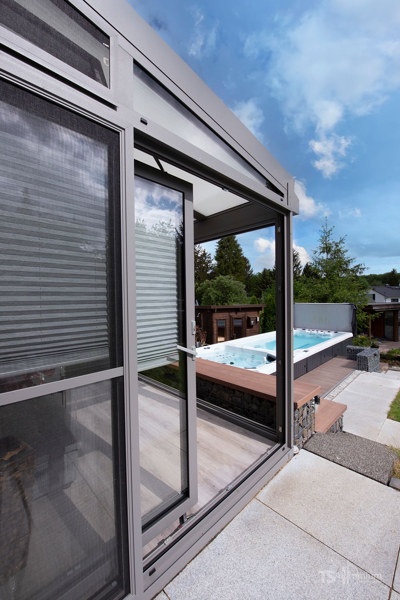 Glasschiebetüren neben einem Gartenpool und einer Terrasse, mit einer teilweise geöffneten Fliegengittertür und blauem Himmel darüber
