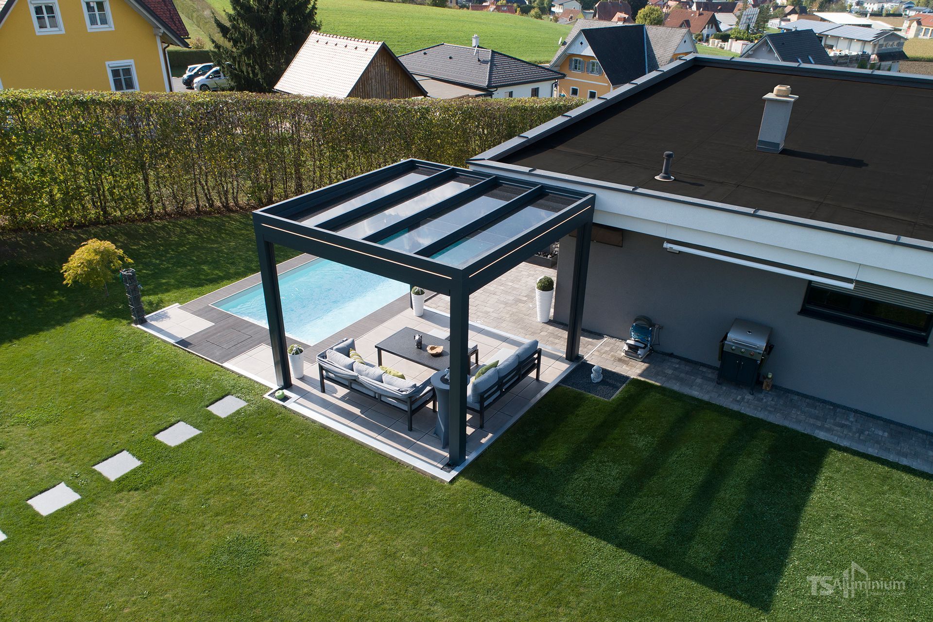 Hinterhofterrasse mit einer modernen Pergola neben einem Haus und einem ordentlich gemähten Rasen.