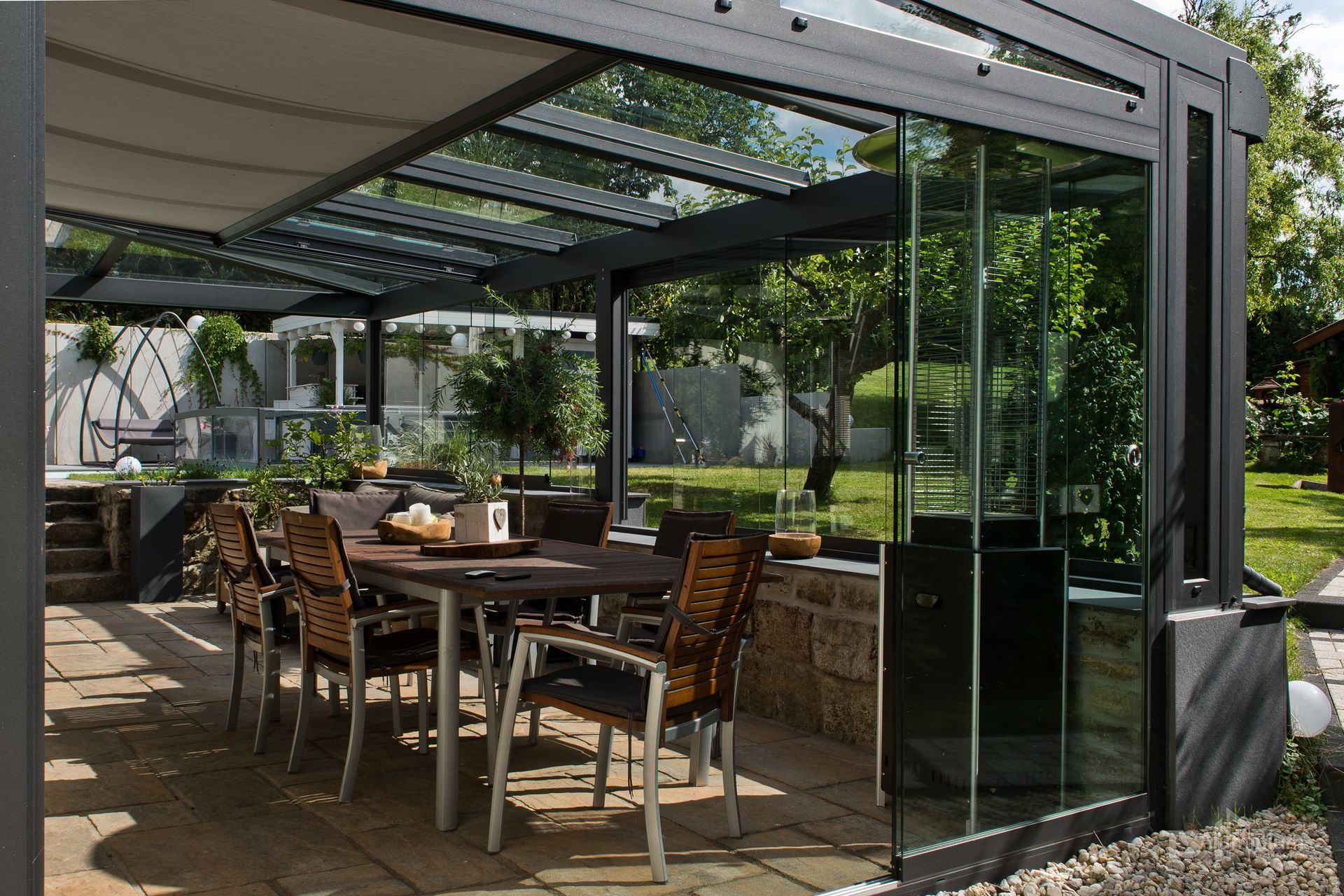 Essbereich auf der Terrasse mit Holztisch und Stühlen unter einer modernen Glaspergola