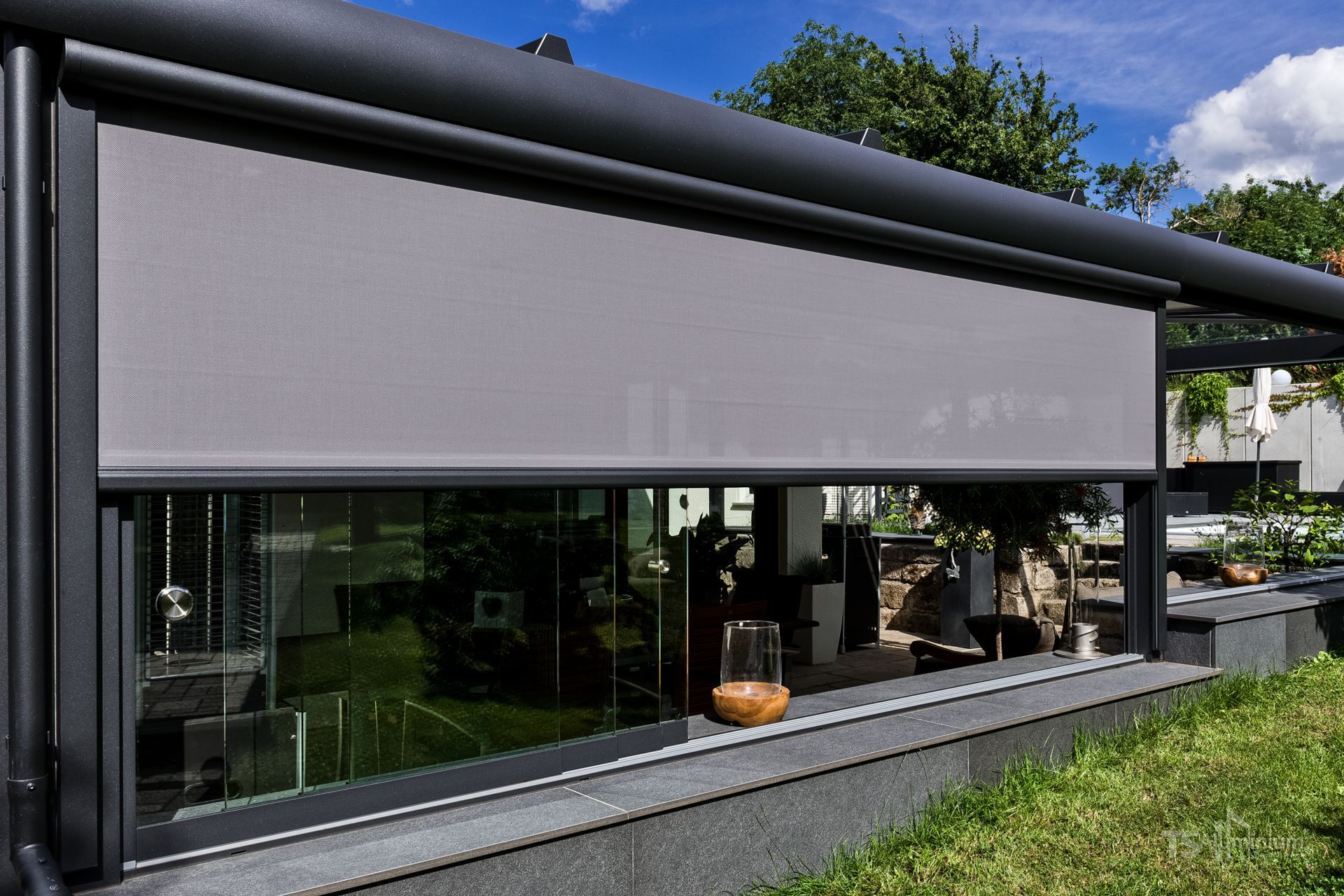 Modernes Haus mit einem großen grauen Fenstervordach und einer Glaswand mit Blick auf einen Garten
