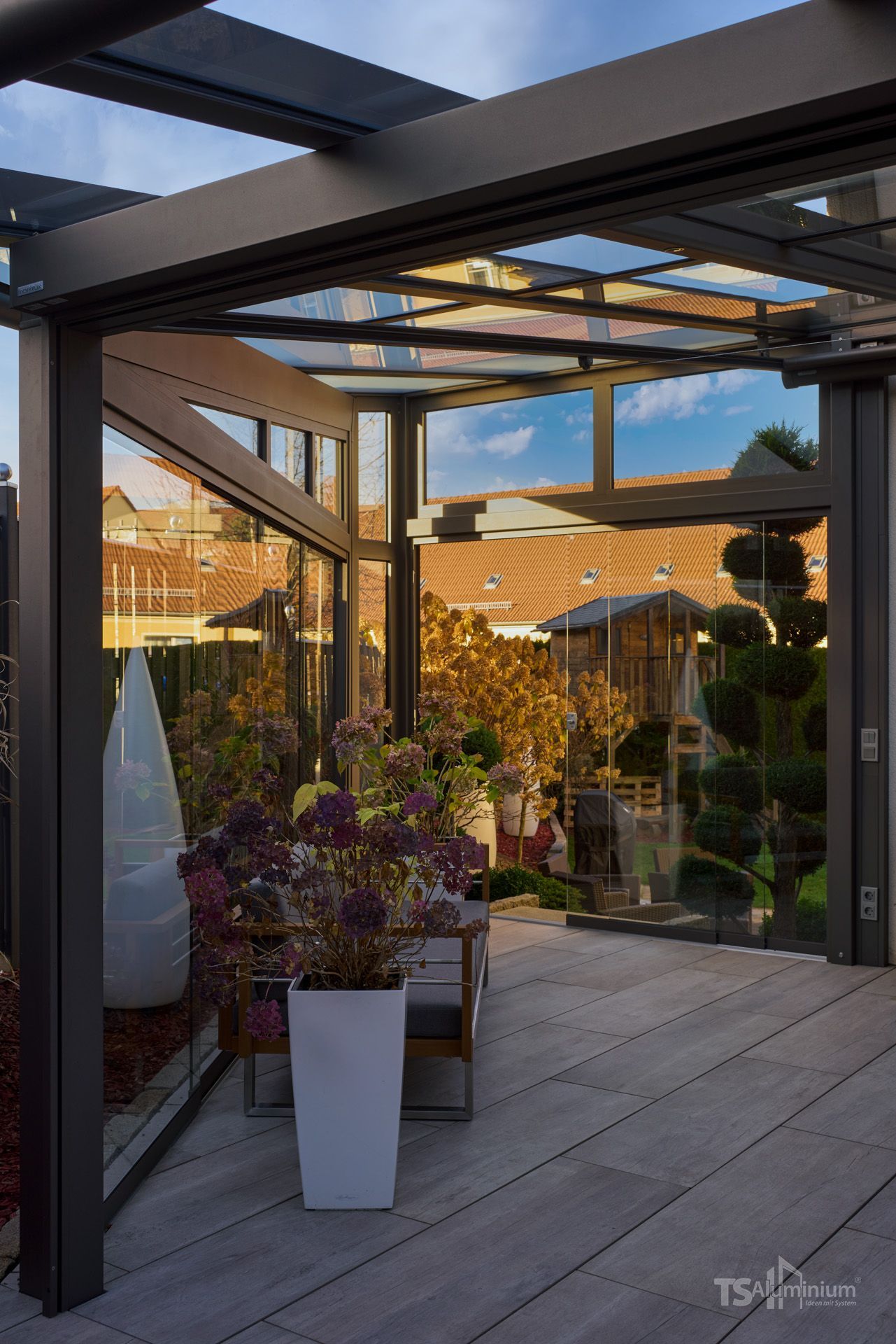 Moderner Patio mit schwarzer Pergola, Topfpflanzen und warmem Sonnenlicht in einem Wohngarten