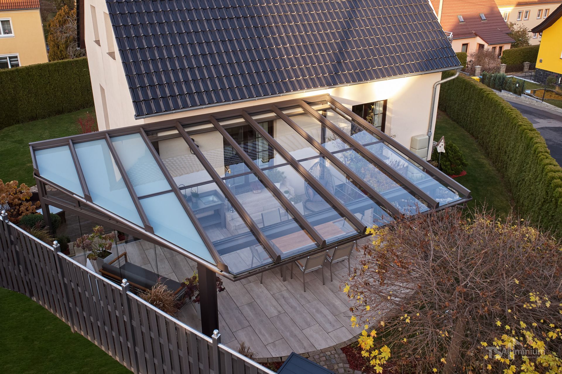 Verglaster Wintergartenanbau im Hinterhof neben einem Haus, mit blauen Solarpaneelen auf dem Dach