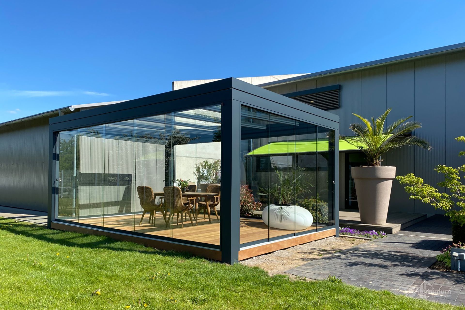 Moderne Terrassenpergola mit Essgruppe neben einer Rasenfläche und einer Topfpflanze an einem sonnigen Tag