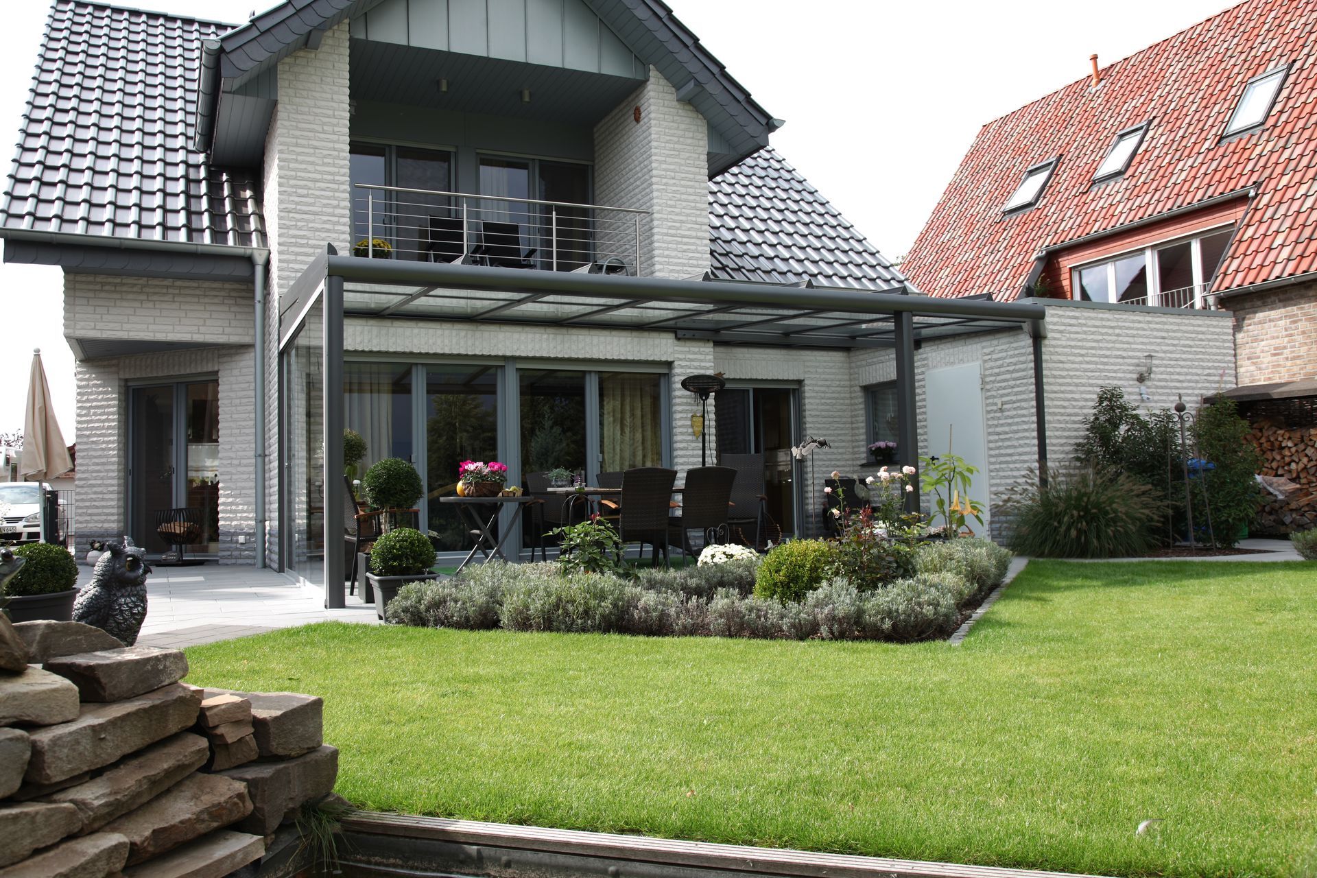 Modernes Haus mit einer Glasterrasse, einem gepflegten Rasen und einer Einfassung aus Naturstein