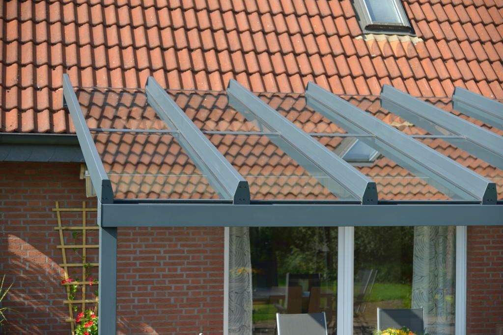 Haus mit rotem Ziegeldach und grauer Metallpergola über einem Terrassenfenster