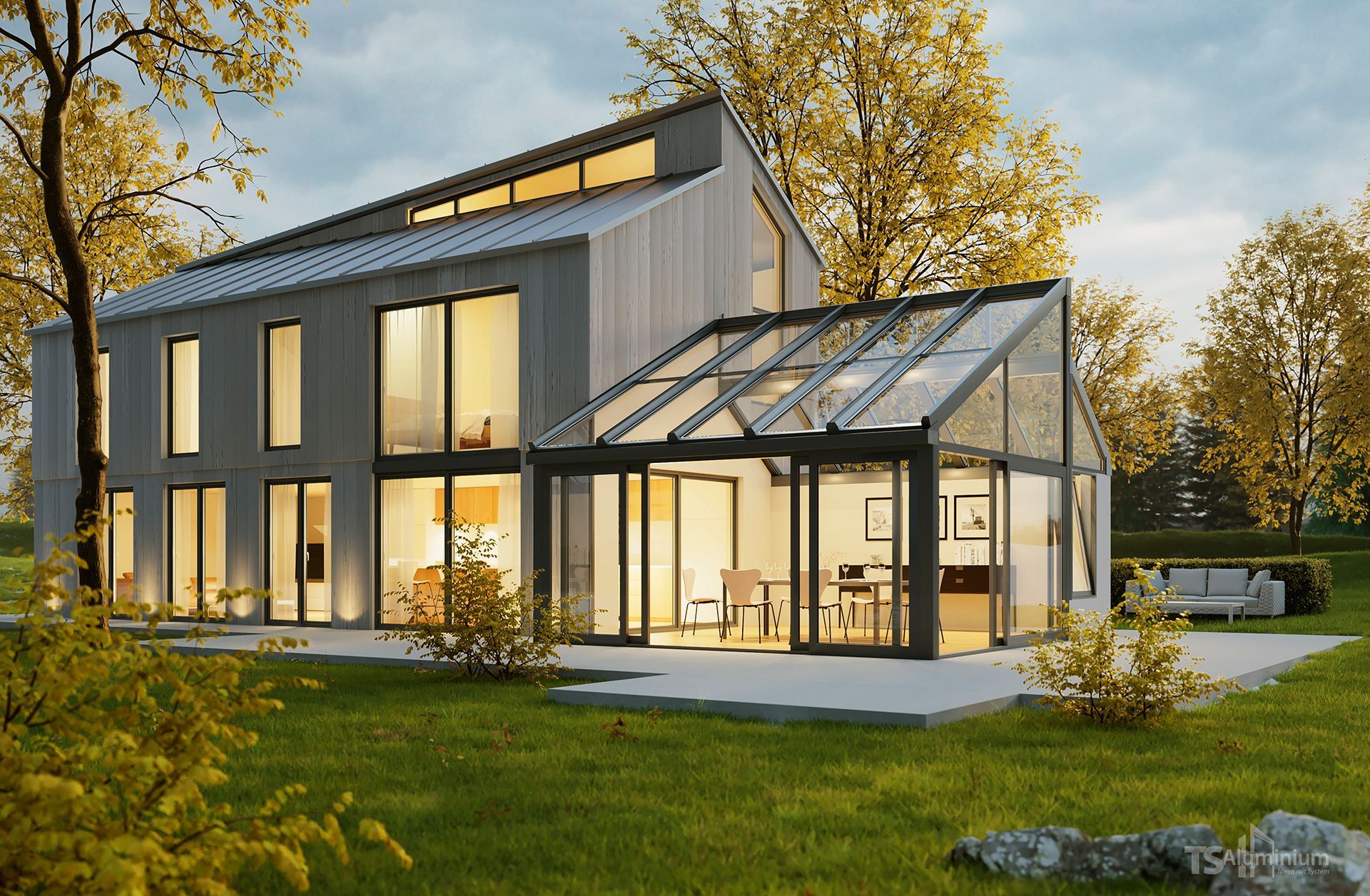 Modernes zweigeschossiges Haus mit Wintergarten aus Glas, beleuchteten Fenstern und herbstlichen Bäumen in der Abenddämmerung