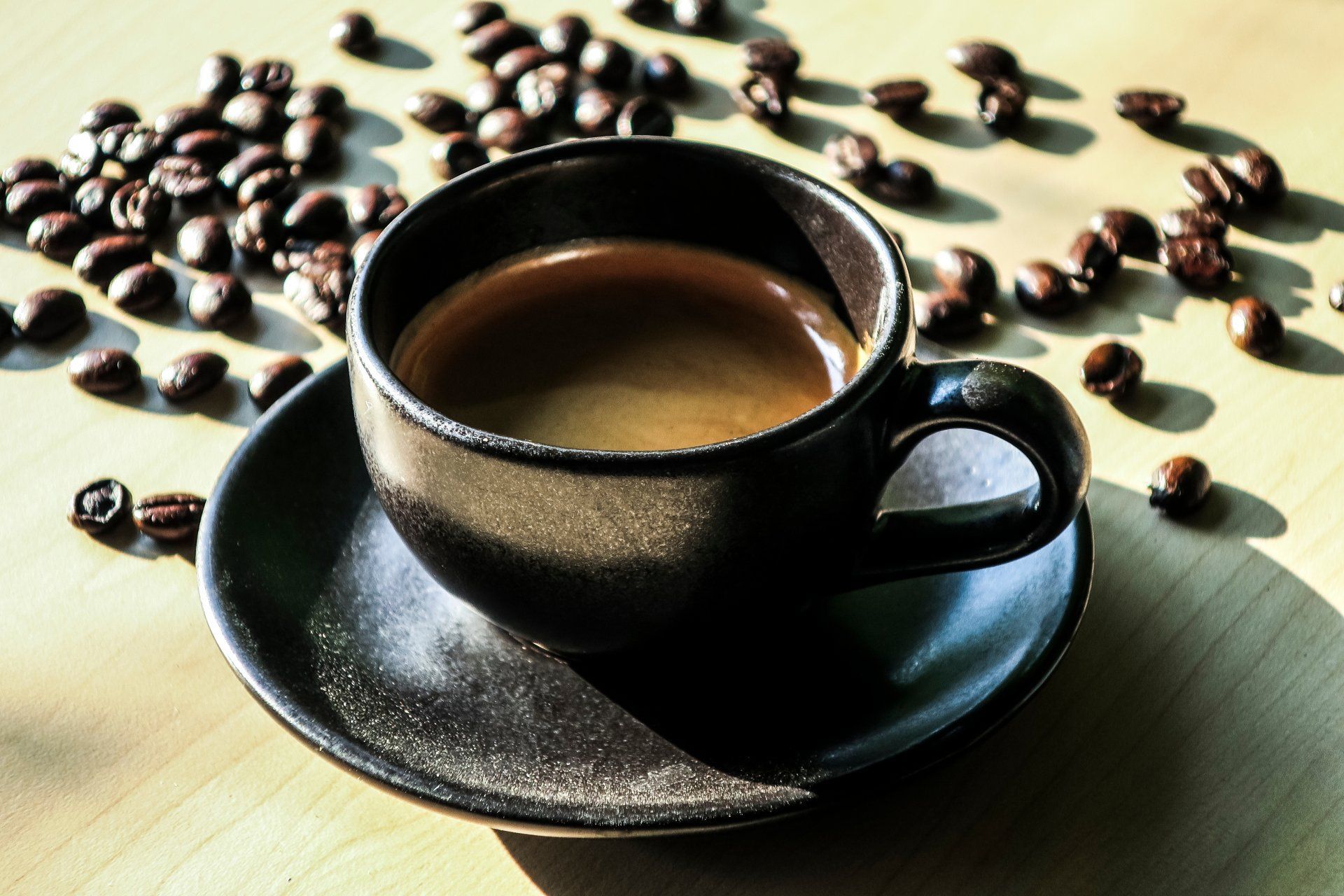 Une tasse de café rempli devant des grains de café.