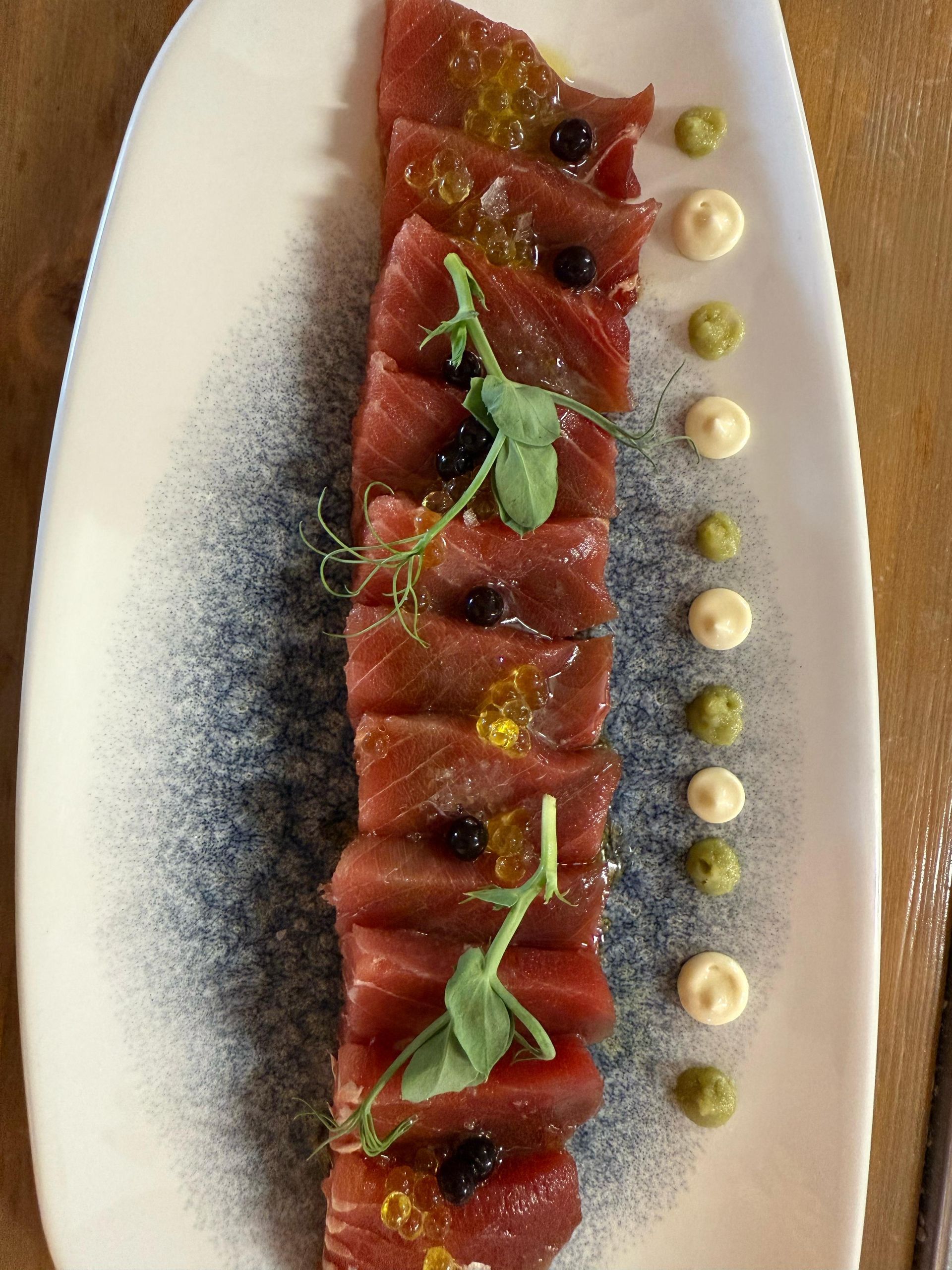Sashimi de atún en un plato blanco, adornado con salsas y verduras.