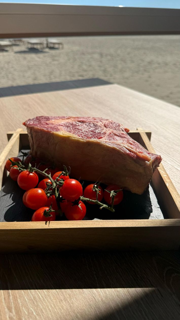 Bistec con tomates cherry en una bandeja de madera, al aire libre, bajo la luz del sol.