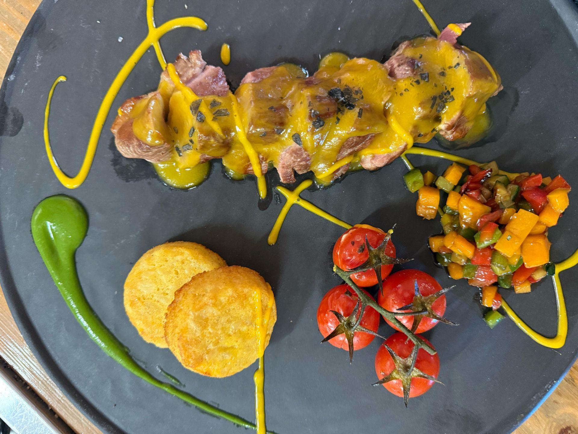 Plato de comida: carne con salsa amarilla, tortas de papa, tomates y vegetales coloridos cortados en cubitos.