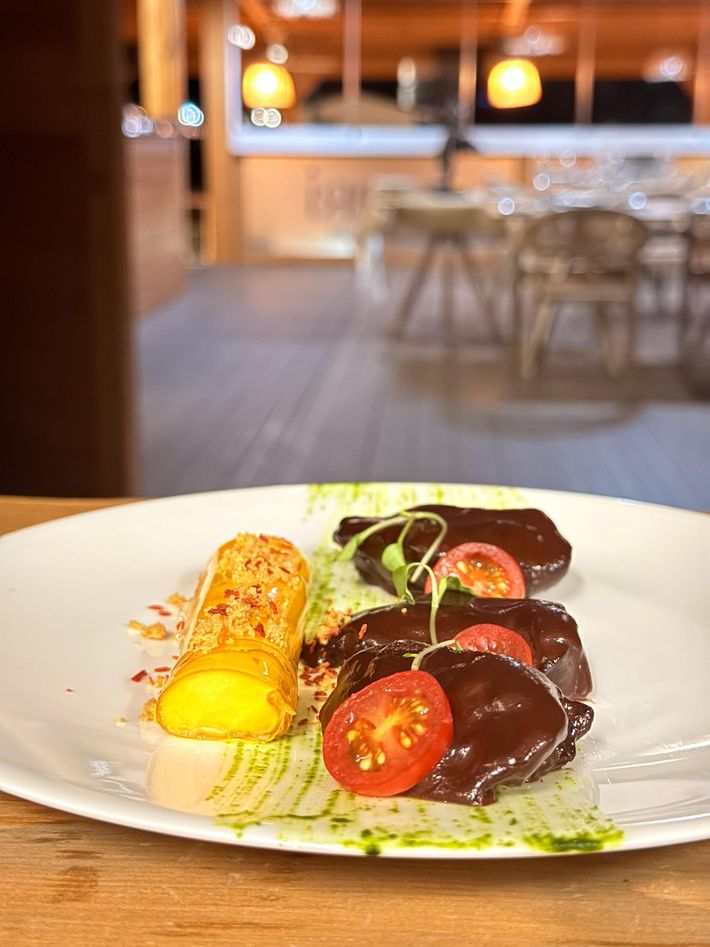 Plato con comida gourmet: carne sellada con tomates cherry y un acompañamiento colorido de comida frita y salsa.
