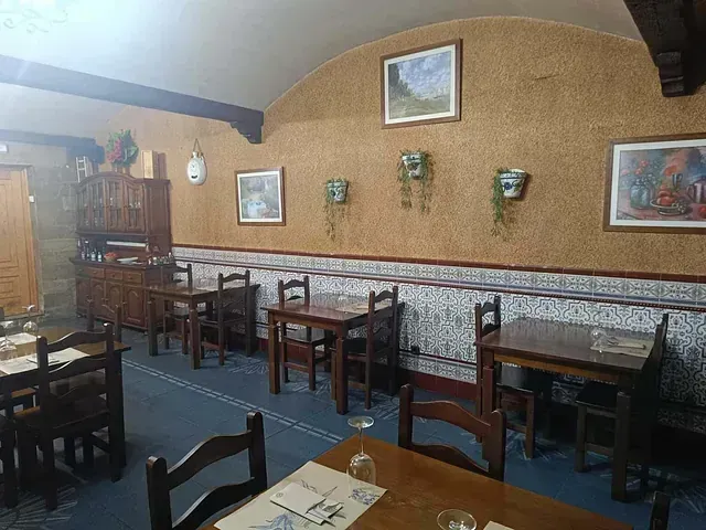 Interior de restaurante con mesas y sillas de madera, decorado con cuadros y plantas colgantes, paredes de azulejos marrones y azules.