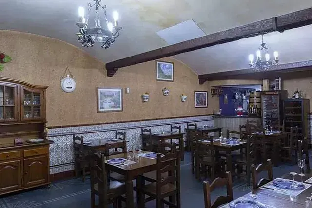 Interior de restaurante con mesas y sillas de madera, barra e iluminación decorativa. Las paredes son de color canela con detalles de azulejos.