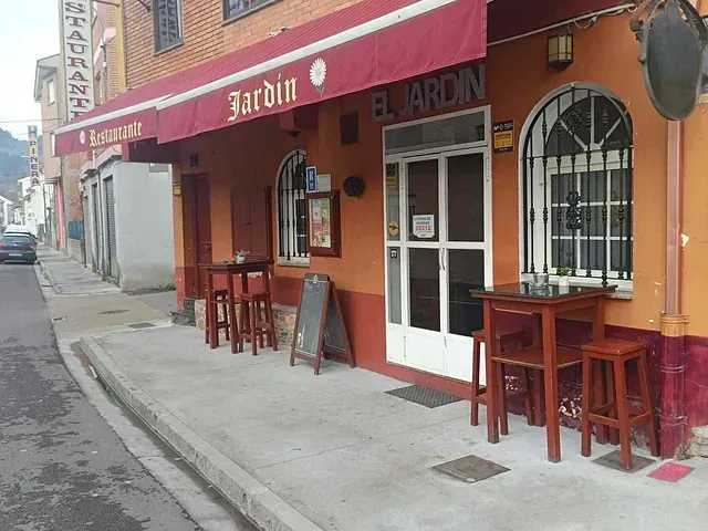 Exterior del restaurante El Jardín en España con toldo rojo, fachada naranja y mesas en la acera.