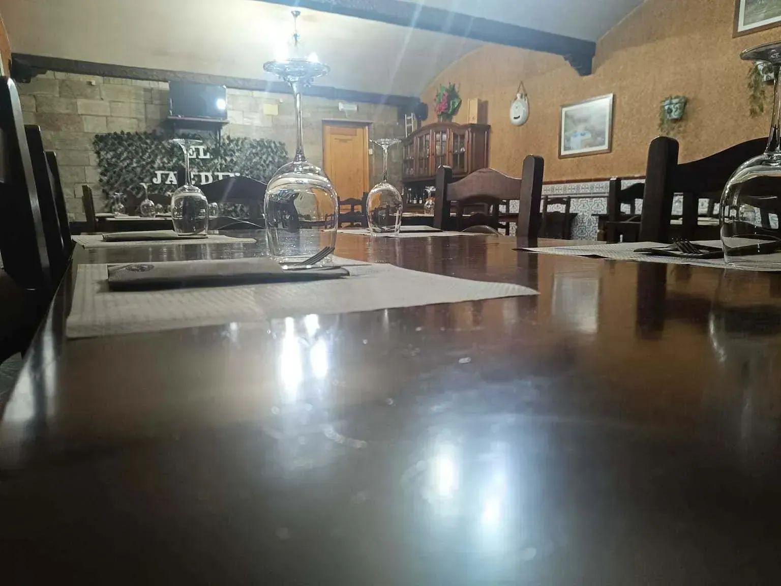 Comedor con una larga mesa de madera preparada para comer, copas de vino y sillas de madera oscura.