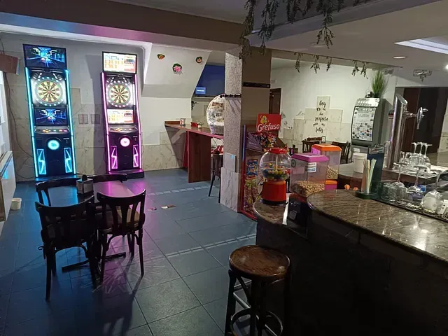 Interior de un bar con máquinas de dardos, mesas, barra y una pequeña sala de juegos. Vacío.